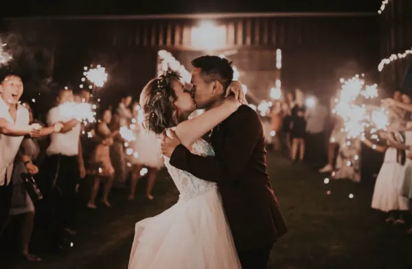 A bride and groom kiss during a sparkler exit at a rustic barn wedding venue.