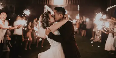 A bride and groom kiss during a sparkler exit at a rustic barn wedding venue.