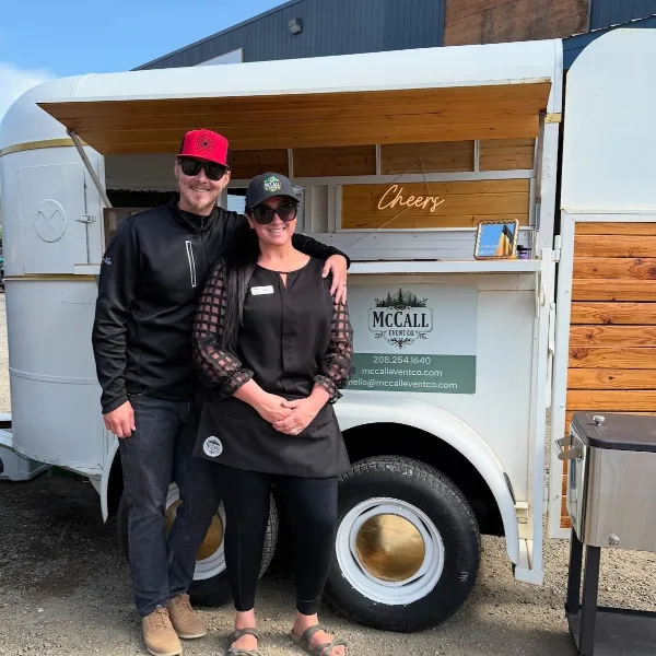 Two people standing in front of a white mobile bar trailer with the McCall Event Co. logo and contact information.