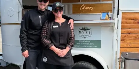 Two people standing in front of a white mobile bar trailer with the McCall Event Co. logo and contact information.