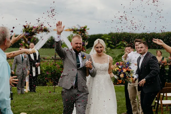 A bride and groom walking down an outdoor aisle while guests throw flower petals.