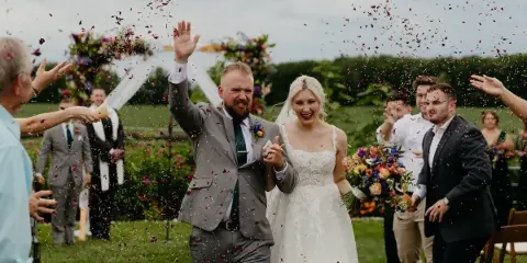 A bride and groom walking down an outdoor aisle while guests throw flower petals.