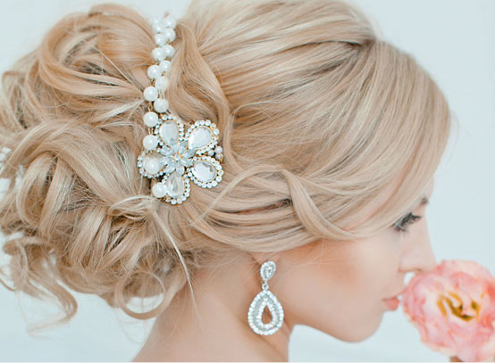 Close-up of a blonde woman's formal updo hairstyle featuring a pearl and crystal hair accessory.