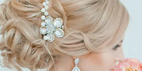 Close-up of a blonde woman's formal updo hairstyle featuring a pearl and crystal hair accessory.