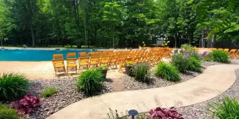 Outdoor wedding ceremony setup with wooden chairs arranged near a pond and forest.