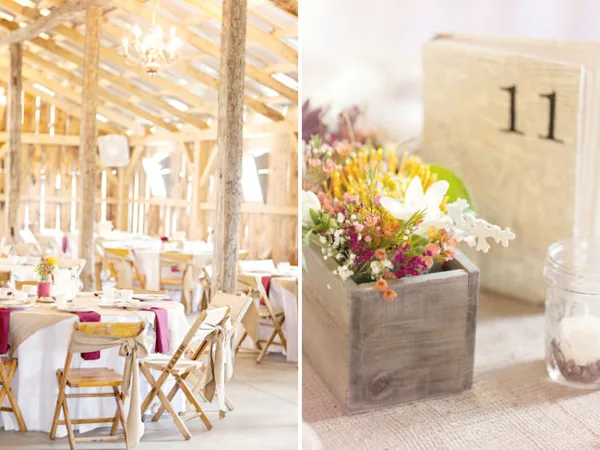 Interior view of a rustic barn wedding venue featuring exposed wooden beams, chandeliers, and set dining tables with white linens and wooden chairs.