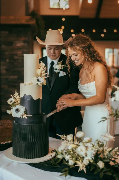 A bride and groom cutting a multi-tiered black and white wedding cake with floral decorations.