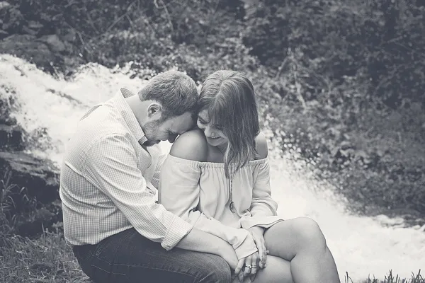 A black and white photograph of a couple sitting together outdoors near a waterfall.