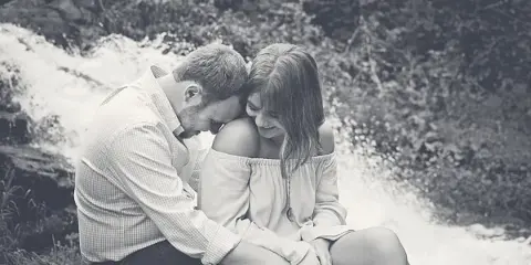 A black and white photograph of a couple sitting together outdoors near a waterfall.
