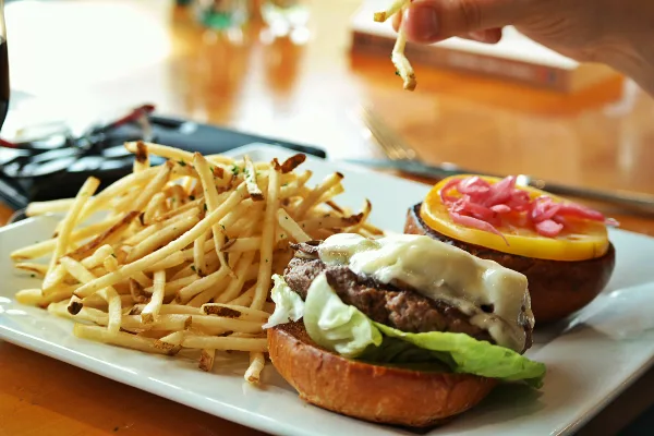 A close-up photograph of a cheeseburger with lettuce and pickled onions served with a side of french fries on a white plate.
