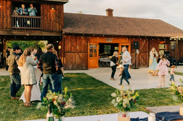 Guests socializing on the lawn and dance floor in front of a rustic wooden barn venue.