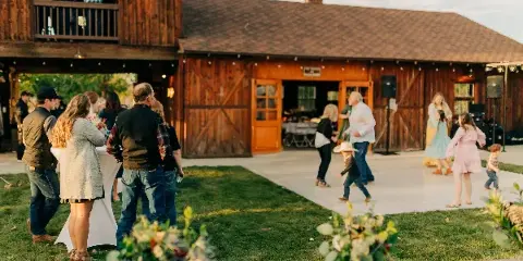 Guests socializing on the lawn and dance floor in front of a rustic wooden barn venue.