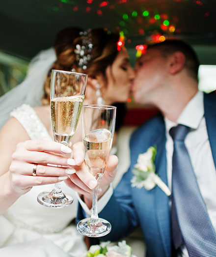 Bride and groom holding champagne flutes while seated inside a limousine.