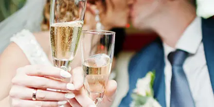 Bride and groom holding champagne flutes while seated inside a limousine.