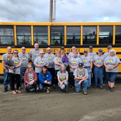 A group of Butler's Bus Service employees posing in front of a yellow school bus.