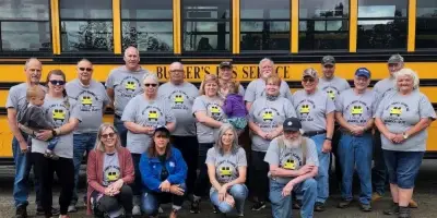 A group of Butler's Bus Service employees posing in front of a yellow school bus.