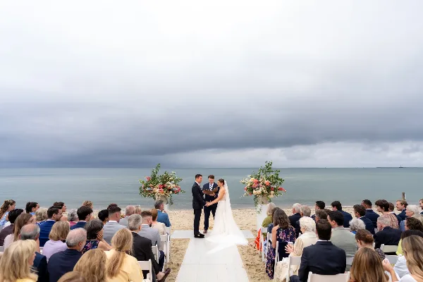 A bride and groom exchanging vows on a beach wedding aisle with guests seated on either side.