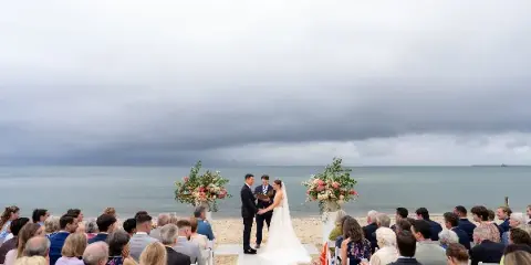 A bride and groom exchanging vows on a beach wedding aisle with guests seated on either side.