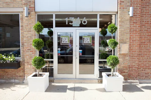 Exterior view of the Loft on Lake venue entrance featuring glass doors, brick walls, and topiary planters.