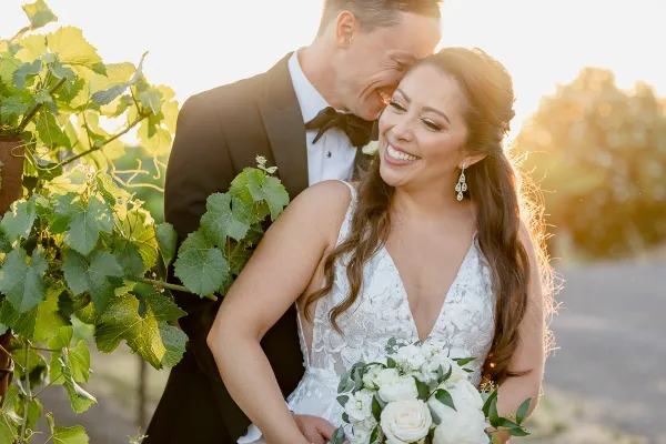 Close-up portrait of a smiling bride with styled hair and soft glam makeup standing next to her groom.