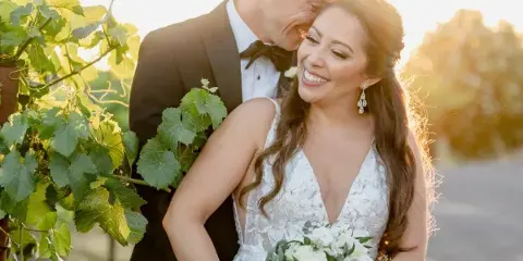 Close-up portrait of a smiling bride with styled hair and soft glam makeup standing next to her groom.