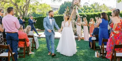 A bride and groom walking down the aisle during an outdoor wedding ceremony with guests seated on either side.