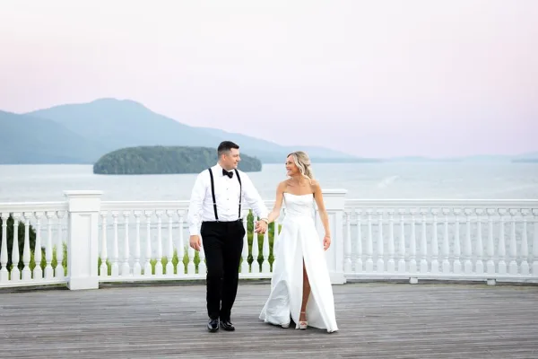 Bride and groom walking on a wooden dock overlooking a lake with mountains in the background.