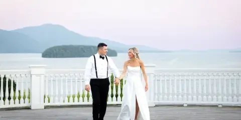 Bride and groom walking on a wooden dock overlooking a lake with mountains in the background.