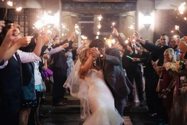 A bride and groom dancing at a wedding reception while guests hold up sparklers.