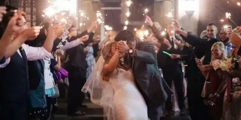 A bride and groom dancing at a wedding reception while guests hold up sparklers.