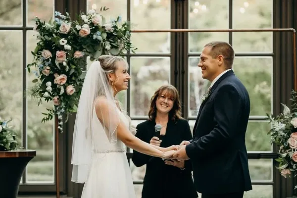 A bride and groom holding hands during a wedding ceremony with an officiant standing between them.