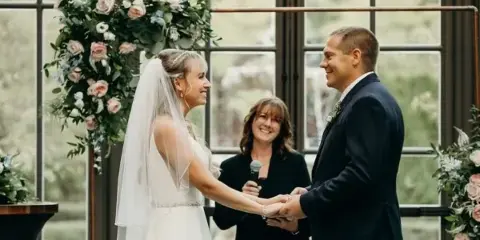 A bride and groom holding hands during a wedding ceremony with an officiant standing between them.