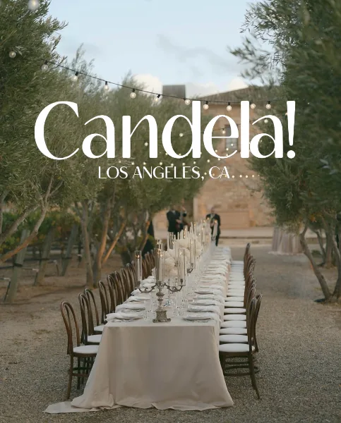 A long wedding reception table set outdoors with string lights and musicians performing in the background.