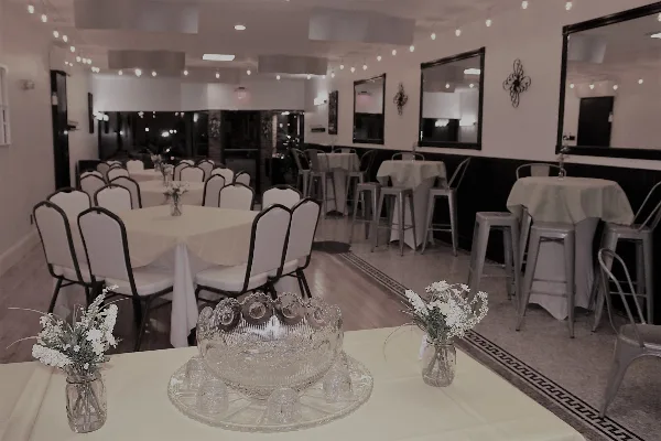 Interior view of an event venue with white tablecloths, chairs, and string lights.