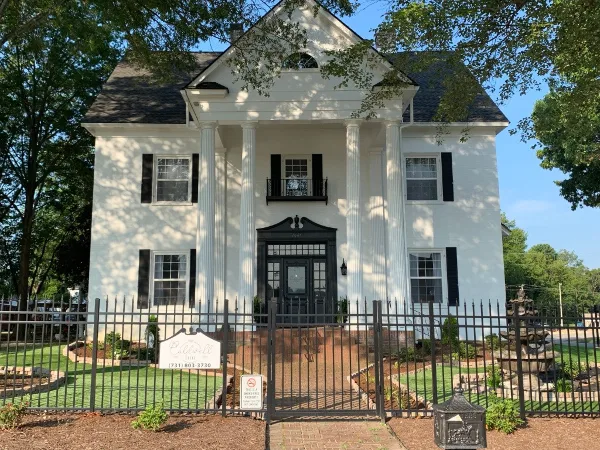 Exterior view of The Caldwell Inn, a white two-story antebellum-style building with a columned portico, black shutters, and a black wrought-iron fence.