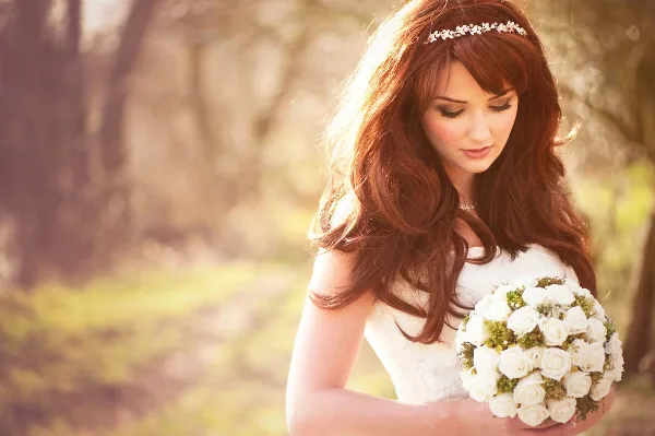 A bride with styled hair and makeup holding a bouquet of white roses.