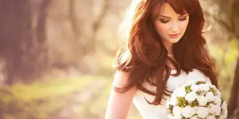 A bride with styled hair and makeup holding a bouquet of white roses.