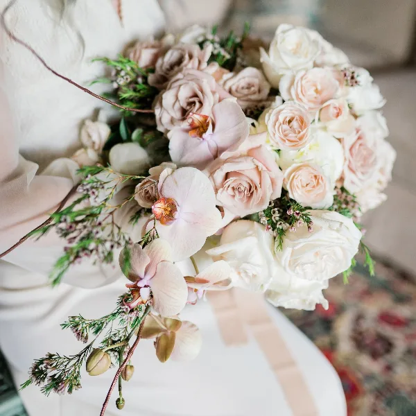 A close-up of a wedding bouquet featuring blush and white roses, pale pink orchids, and greenery.