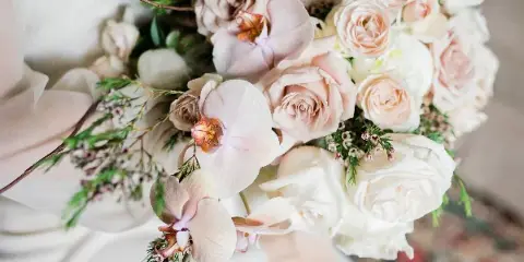 A close-up of a wedding bouquet featuring blush and white roses, pale pink orchids, and greenery.