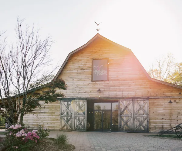 Exterior view of a rustic wooden barn with a weathervane and the Arabella Farm sign on the gable.