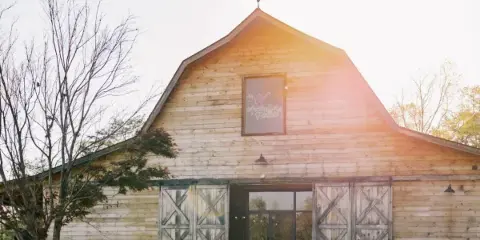 Exterior view of a rustic wooden barn with a weathervane and the Arabella Farm sign on the gable.