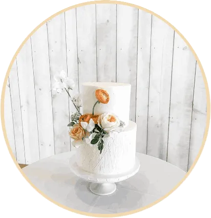 A two-tier white wedding cake decorated with white and peach roses on a white cake stand.