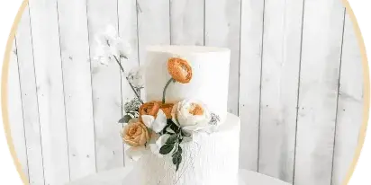 A two-tier white wedding cake decorated with white and peach roses on a white cake stand.