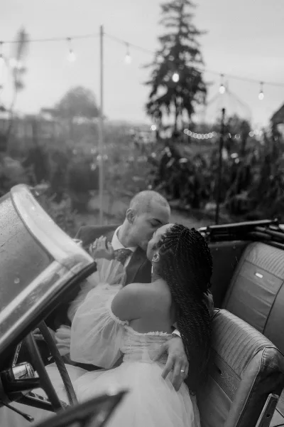 A black and white photograph of a bride and groom kissing in a convertible car.