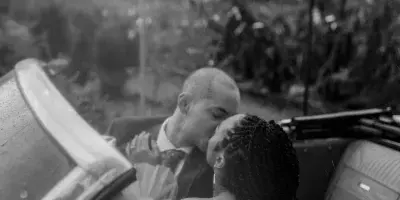 A black and white photograph of a bride and groom kissing in a convertible car.