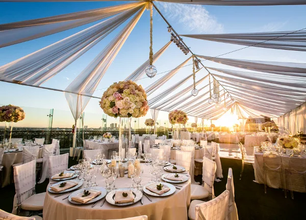 Wedding reception set up inside a draped white tent with round tables, white chair covers, linens, and floral centerpieces.