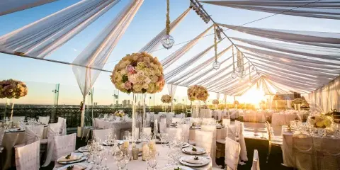 Wedding reception set up inside a draped white tent with round tables, white chair covers, linens, and floral centerpieces.