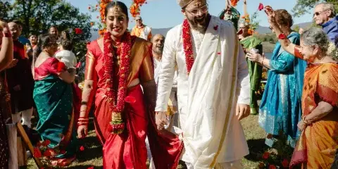 A couple in traditional Indian wedding attire walking through a crowd at an outdoor wedding reception, featured on a Wezoree magazine cover.
