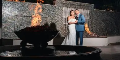 A bride and groom standing together at an outdoor wedding venue with a fire feature.