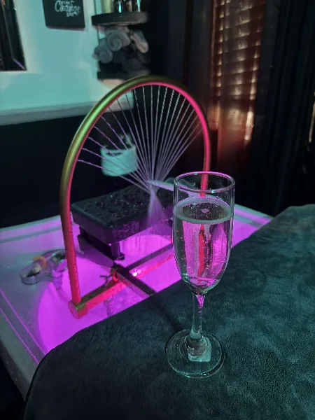 Interior view of a beauty salon showing a treatment chair, a glass of champagne, and a towel under purple ambient lighting.